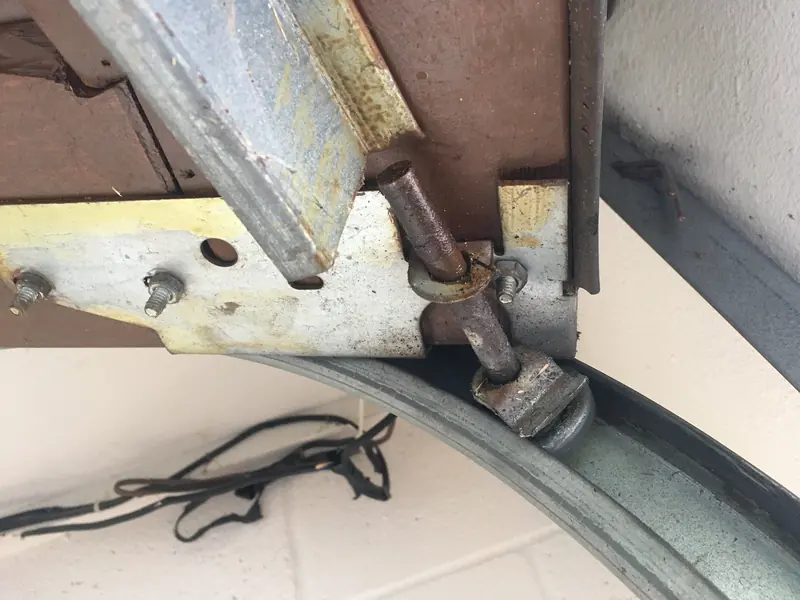 Worn garage door roller with a bent stem in the curved track, next to the top bracket